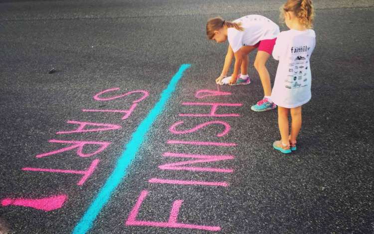 Young girls paint a start/finish line on the pavement.