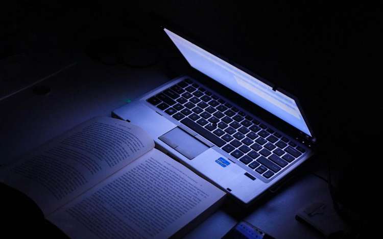 A laptop illuminates a book in a dark room.