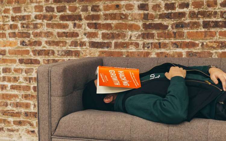 A person naps on a couch with a book over their face.