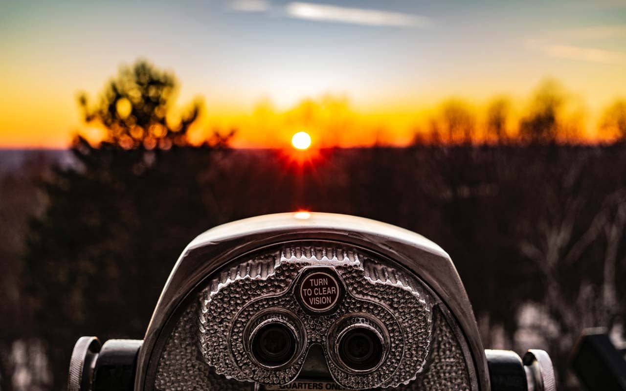 A tower viewer (binoculars on a stand) overlooks an out of focus horizon at sunset.