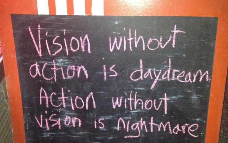 A chalkboard sign outside a cafe reads, "Vision without action is daydream. Action without vision is nightmare."