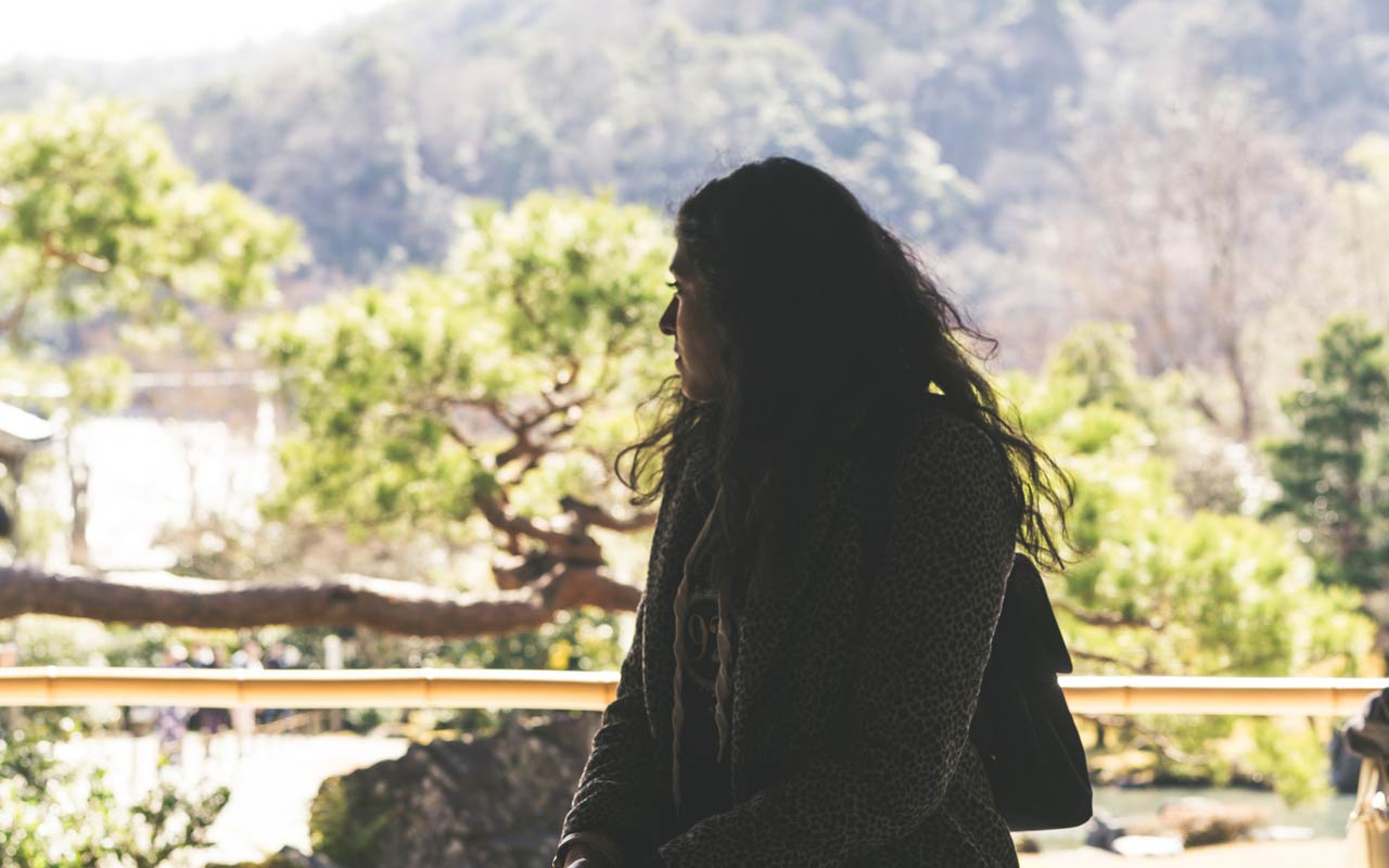 A woman sits, looking out over a remote lake. Meditation can help you focus your mind.