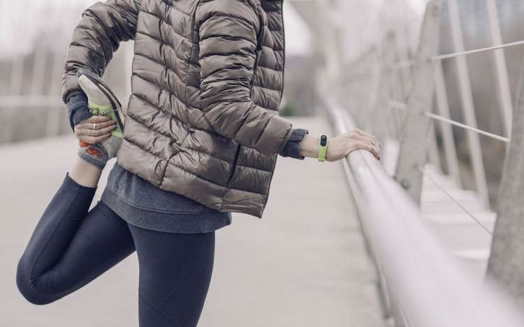 A woman in a puffy jacket stretches out her legs before running. The quality of your brain cells directly correlates to the health of your mind.