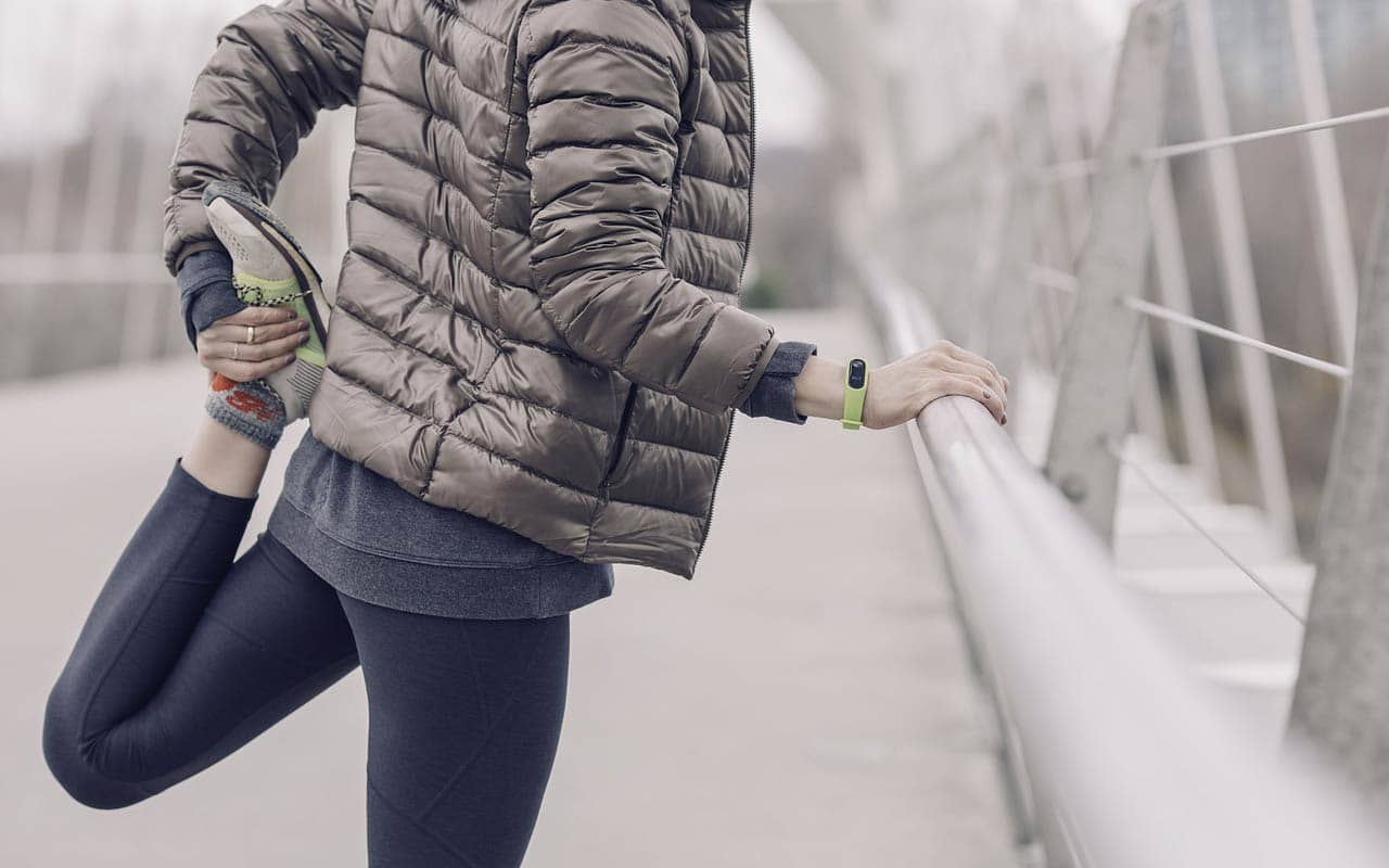 A woman in a puffy jacket stretches out her legs before running. The quality of your brain cells directly correlates to the health of your mind.