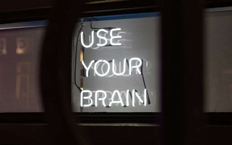 A white neon sign against a black background reads "USE YOUR BRAIN."