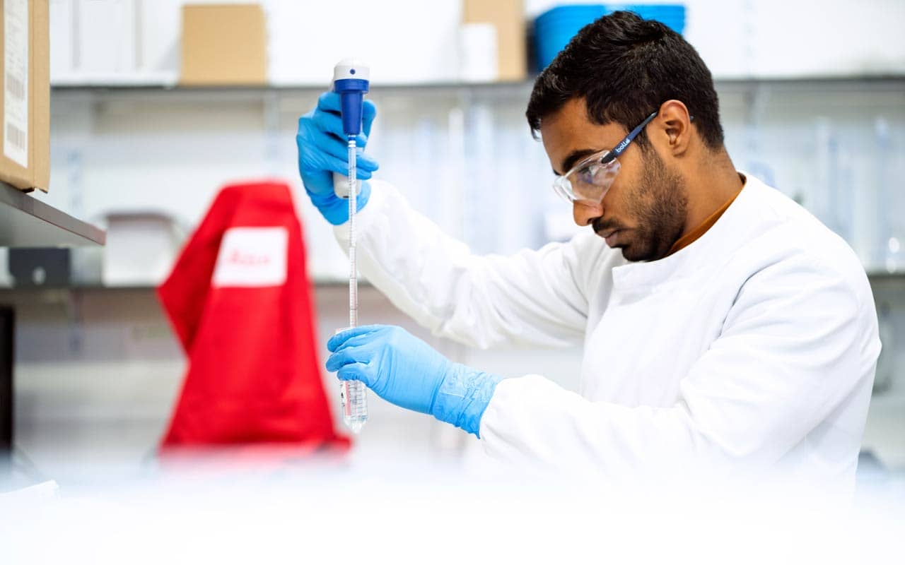 A scientist carefully moves liquid into a test tube with a pipette.