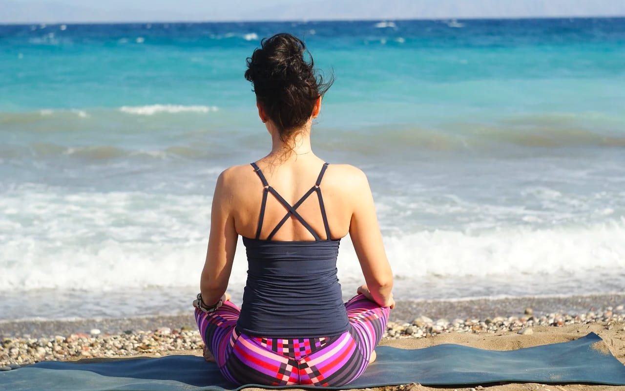 a woman is meditating on a beach
