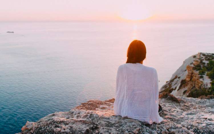 a women is sitting beside an ocean and doing mental imagery