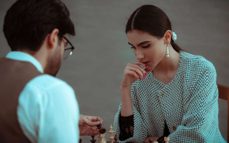 long hair woman and glasses man are playing chess