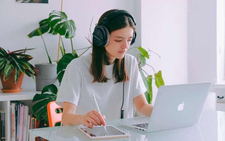 a girl is writing on her laptop with headphones