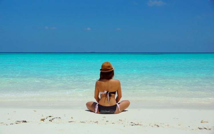 woman wearing a brown hat is meditating on a beach