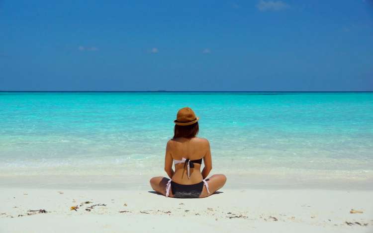 woman wearing a brown hat is meditating on a beach