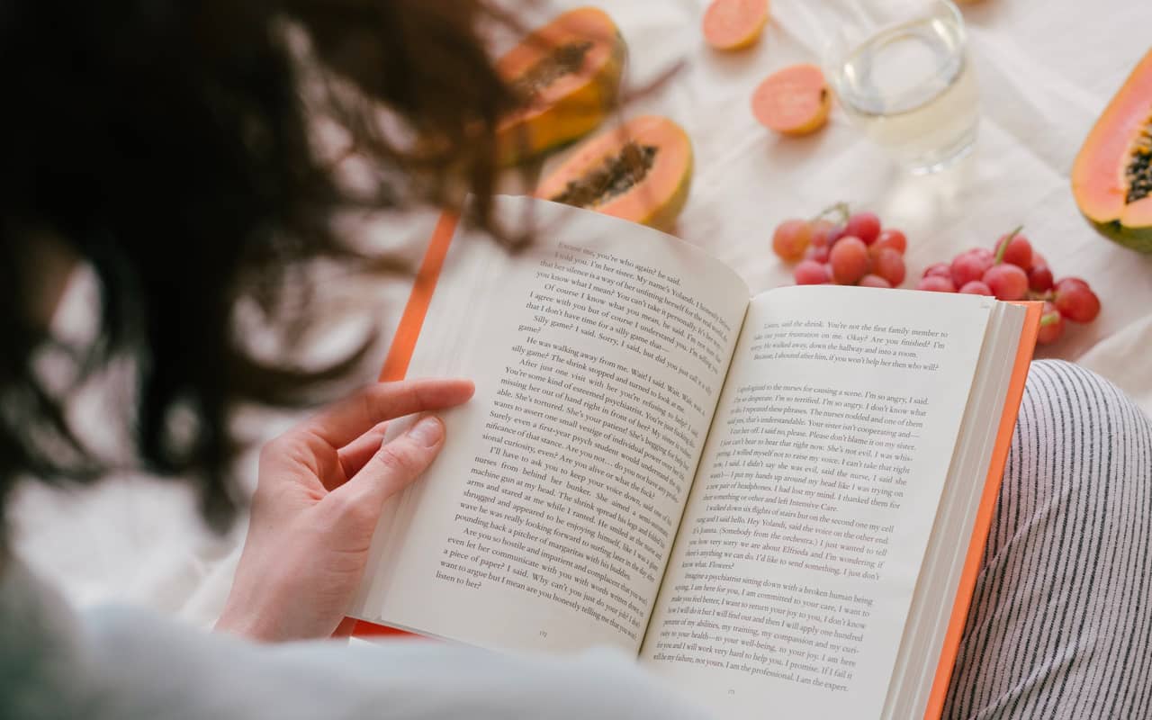 a woman is reading a book with some fruits around