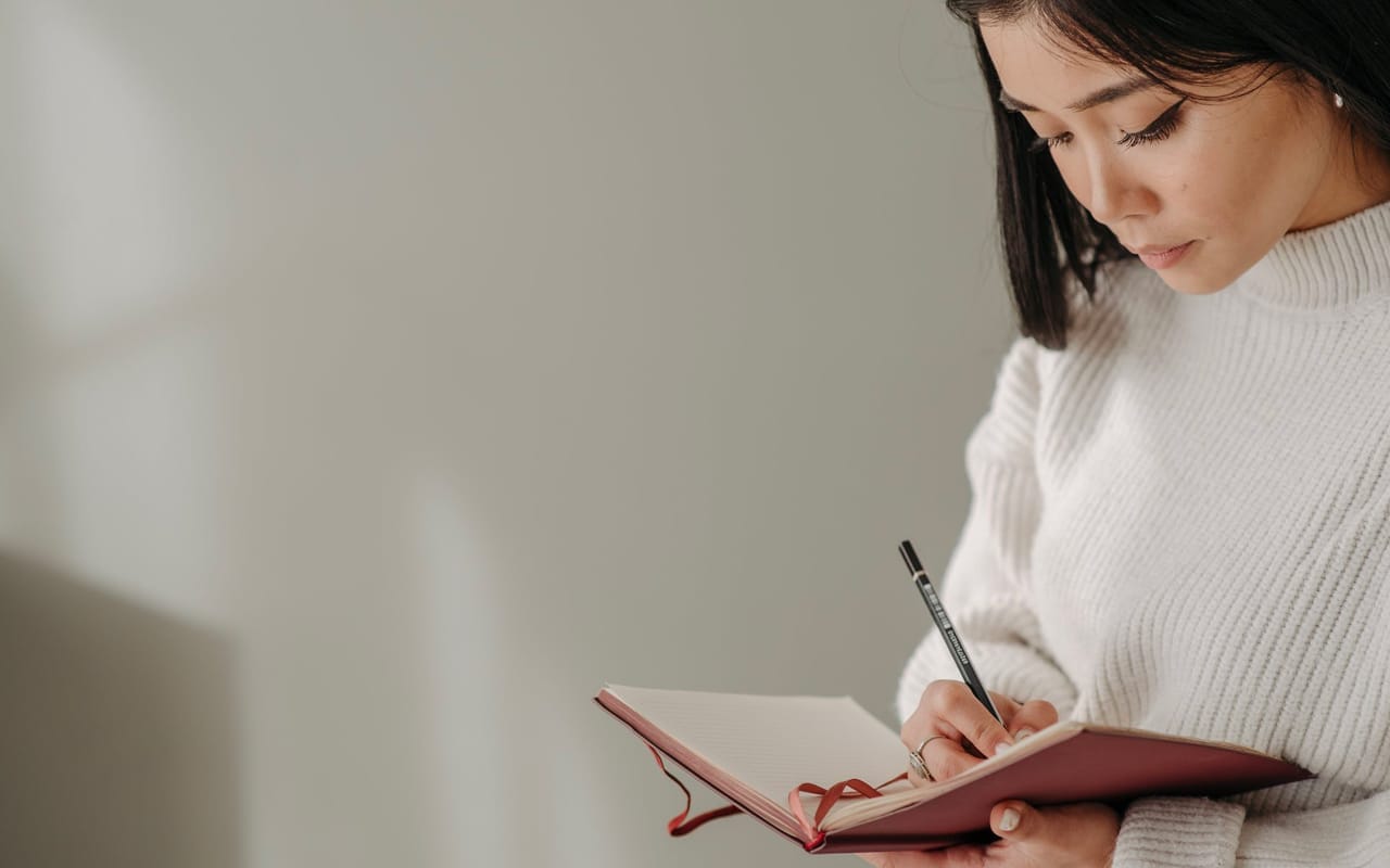 a woman is writing on a pink book