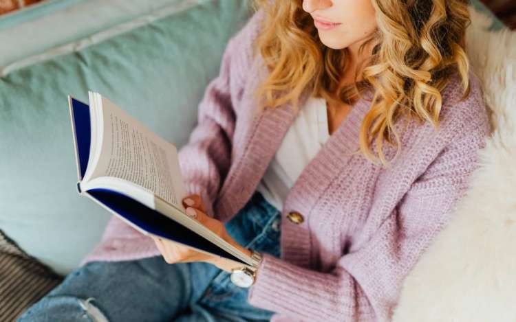 pink sweater woman is reading on a sofa