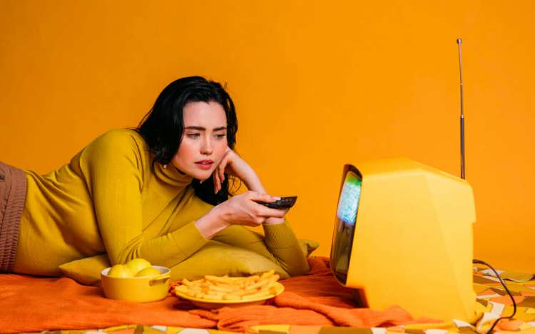 a woman is watching tv with yellow orange background