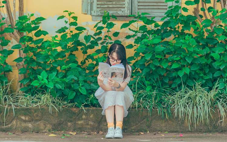 young girl reading in front of green plants
