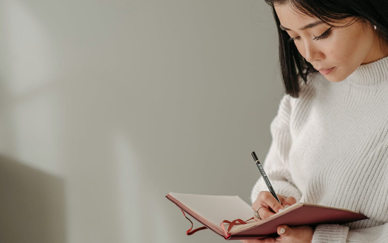 a woman is writing notes on a pink note book