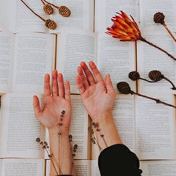 how to become a polymath feature image of hands over a variety of open books with herbs and plants